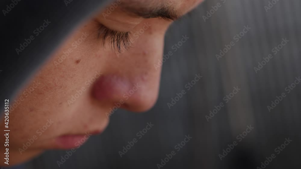A closeup shot of the eyes of a.young, sad and depressed looking teenage boy sitting alone in a dark garage looking at a photograph.