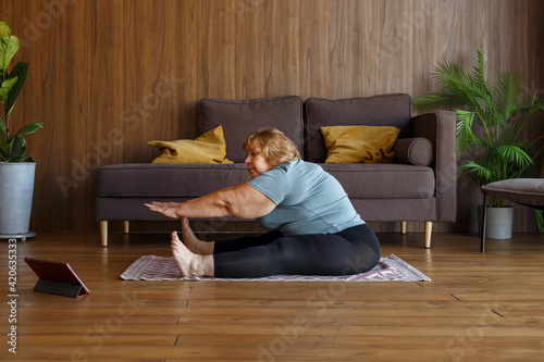 Overweight mature woman stretching during online yoga lesson photo