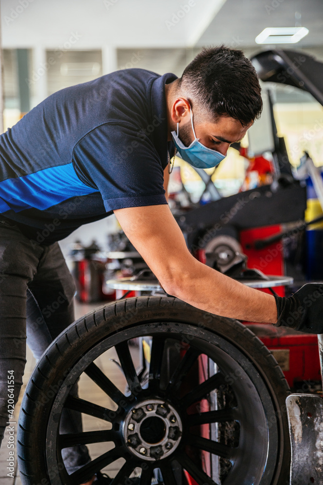 Mechanic in mask working with car wheel Mechanic in mask working with car wheel
