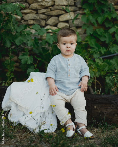 Cute baby in muslin clothes sits on log.