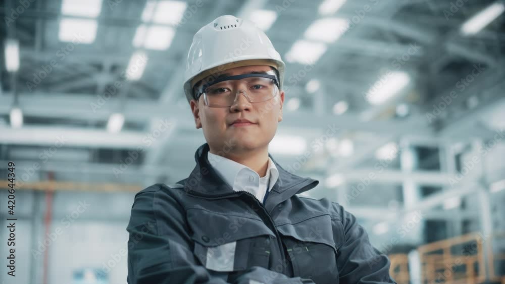 Portrait of a Professional Asian Heavy Industry Engineer/Worker Wearing Safety Uniform, Glasses and Hard Hat. Confident Chinese Industrial Specialist Standing in a Factory Facility. Portrait of a Professional Asian Heavy Industry Engineer/Worker Wearing Safety Uniform, Glasses and Hard Hat. Confident Chinese Industrial Specialist Standing in a Factory Facility.