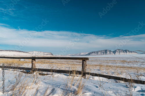 old part of the fence in the steppe in winter against the background of the mountain