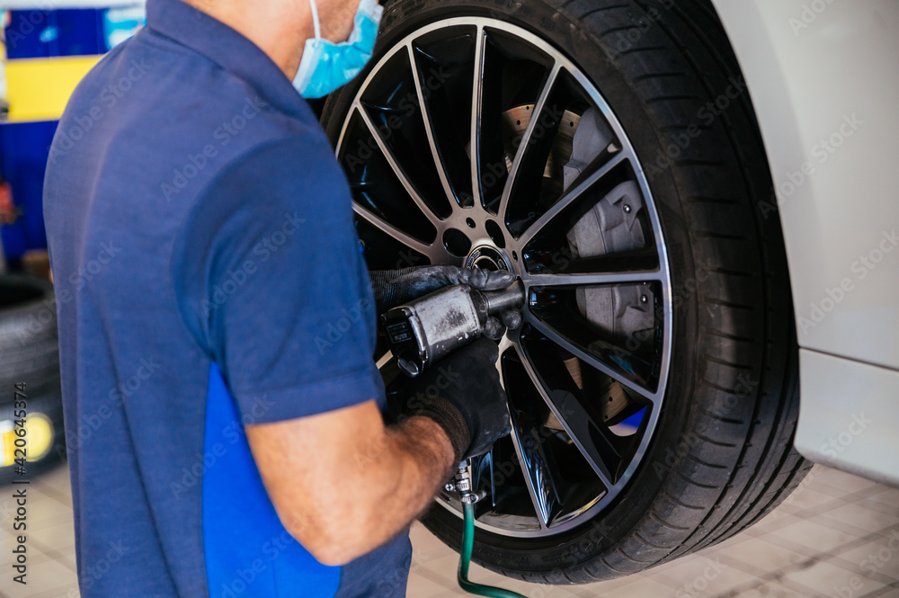 Mechanic in mask screwing wheel to car Mechanic in mask screwing wheel to car