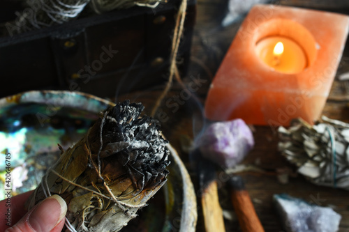 A close up image of a burning white sage smudge stick and healing crystals. 