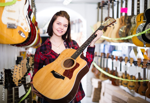 Nice teen girl examining various acoustic guitars in guitar shop