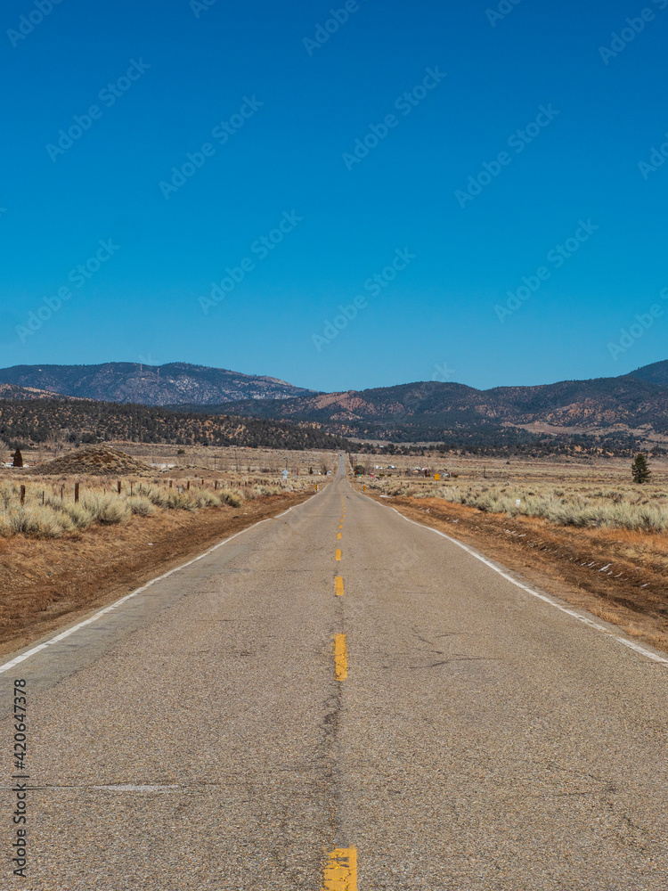 Looking Down The Middle Of A Long Asphalt Country Road Towards Mountains Looking Down The Middle Of A Long Asphalt Country Road Towards Mountains