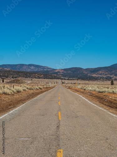 Looking Down The Middle Of A Long Asphalt Country Road Towards Mountains