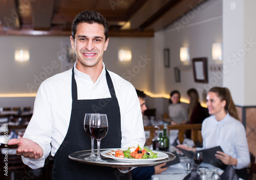 happy waiter with serving tray welcoming to cozy restaurant