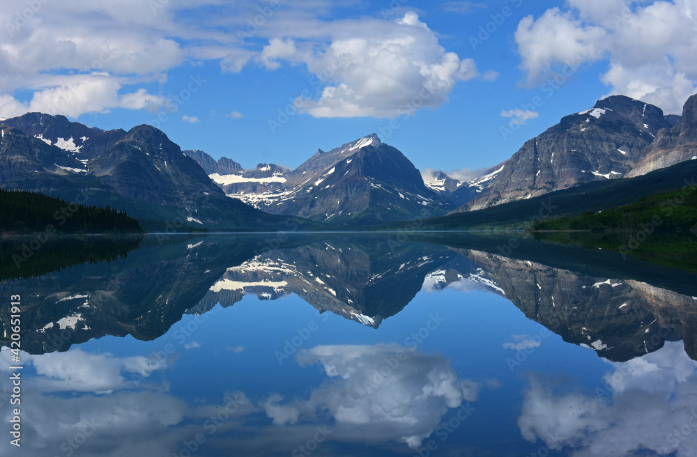 the reflection of  mountain peaks in glacier park national park, montana, in the mirrorlike surface of lake sherburne im the many glacier valley along the road to many glacier in the summer