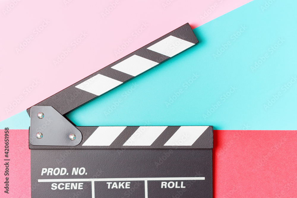 Naklejka premium The clapper board on pink, red and blue background close-up.