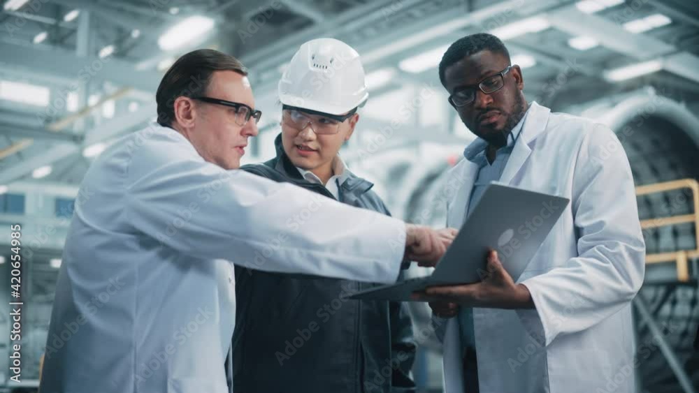 Team of Diverse Professional Heavy Industry Engineers Wearing Safety Uniform and Hard Hats Working on Laptop Computer