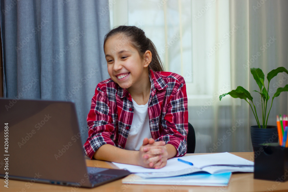 Smiling brunette girl, dressed in a red shirt, sits at home studying, writes homework, communicates on the Internet at the computer. Smiling brunette girl, dressed in a red shirt, sits at home studying, writes homework, communicates on the Internet at the computer.