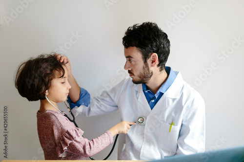 Young doctor examines a child while the kid is allowed to use his stethoscope.