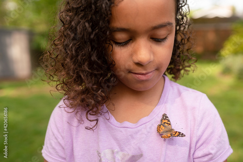 Girl cautiously glances down at butterfly on her chest photo