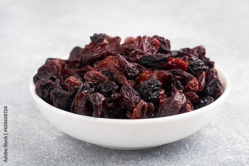 Dried raisins from dark grapes in a plate on a gray concrete background, copy space. top view