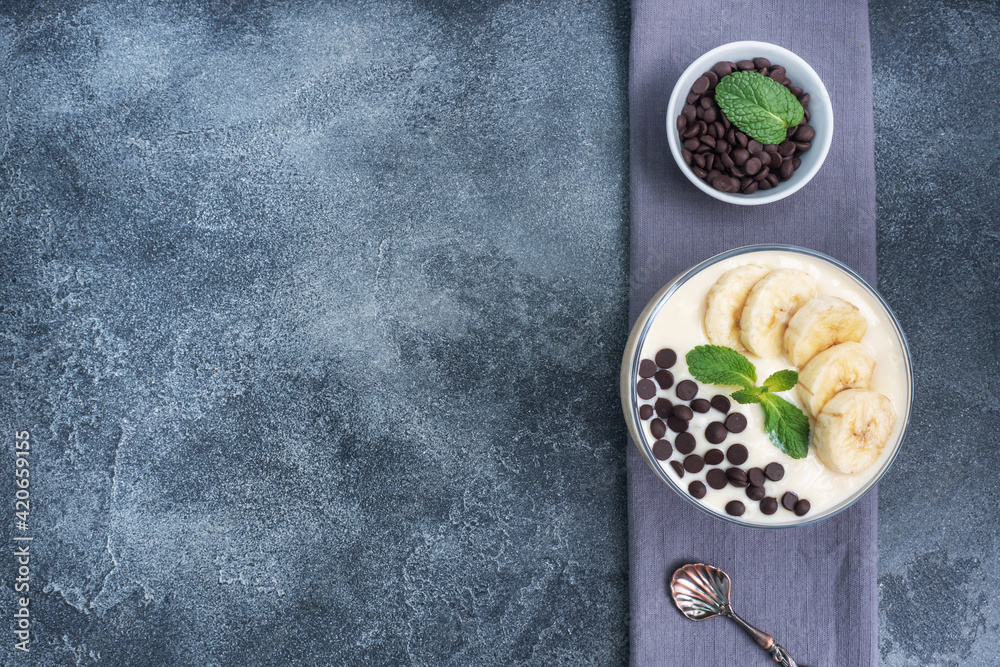 Healthy breakfast, dessert with milk yogurt banana and chocolate on a plate. Dark concrete background. Top view, copy space.