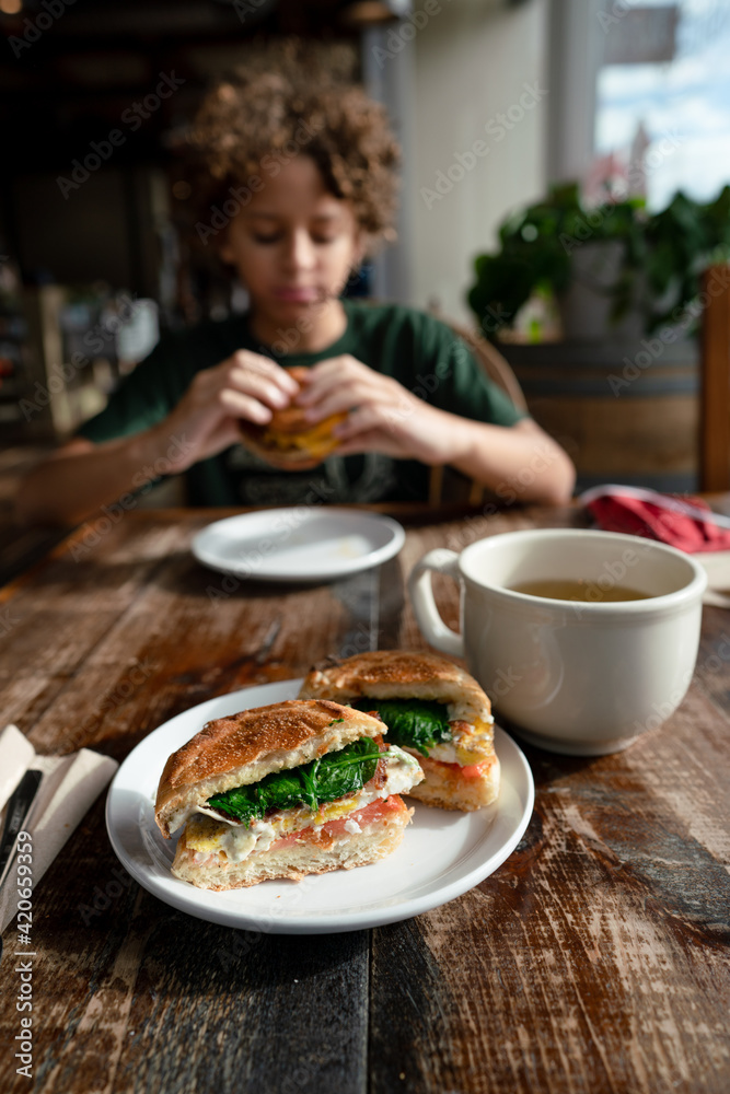 Breakfast sandwich at cafe table across from eating child Breakfast sandwich at cafe table across from eating child