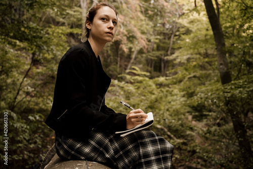 Young woman sitting and drawing in notebook in forest during autumn