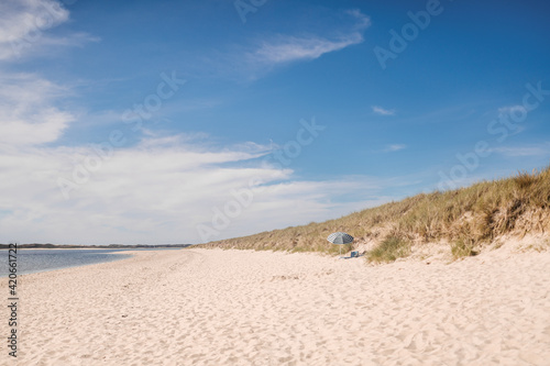 Sandy beach with parasol on sunny day photo