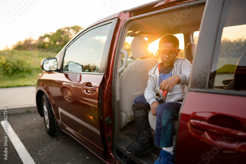 Boy with walking boot looks out open minivan door photo