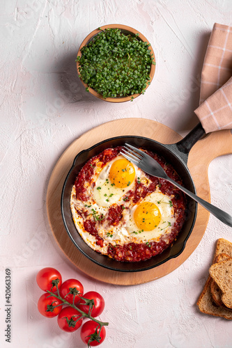 Flat lay image of shakshouka in a pan on a light coloured background photo