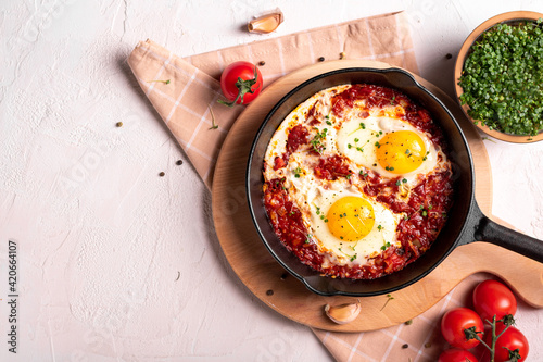 Flat lay image of shakshouka in a pan on a light coloured background photo