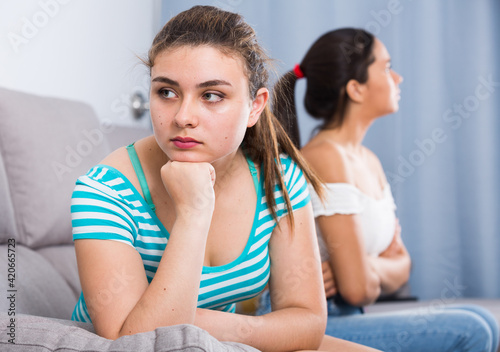 Two quarreled girls teenagers ignoring each other on sofa at home