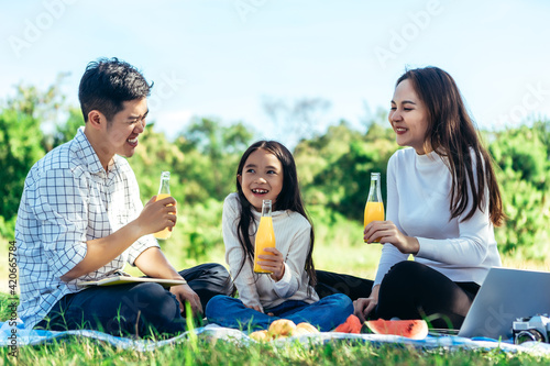 happy Asian family is having picnic in garden and drinking Orange juice in bottle with their daughters on holiday happily.