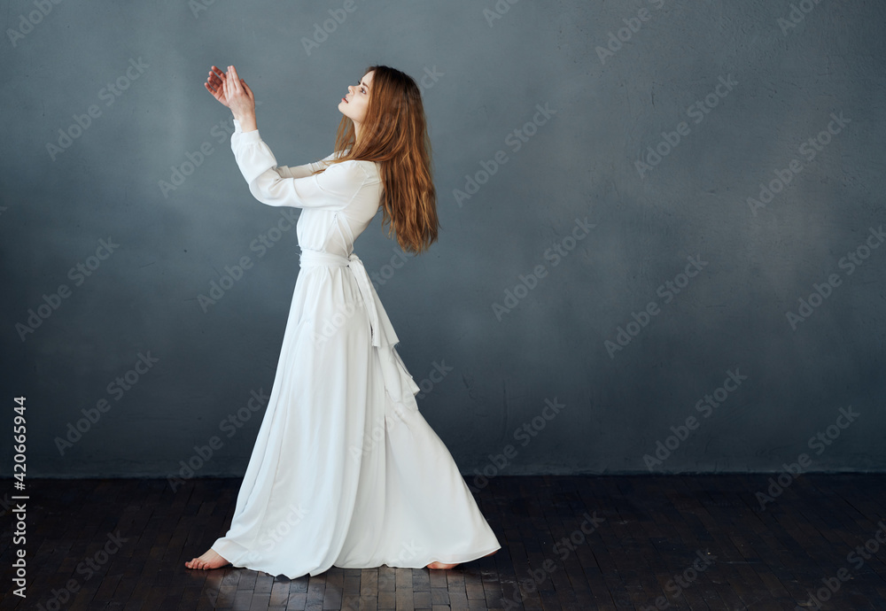 Beautiful woman in a white dress to the floor on a gray background in full growth Beautiful woman in a white dress to the floor on a gray background in full growth