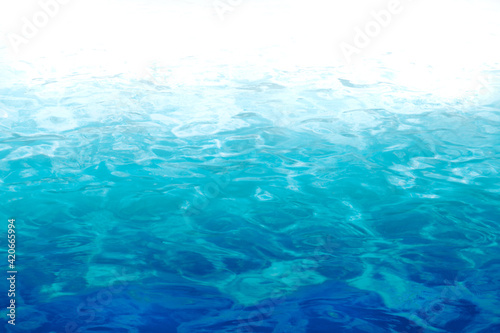  Water in a pool with slightly moving waves and reflections of the sun, gradient from dark to light blue to white with copy-space