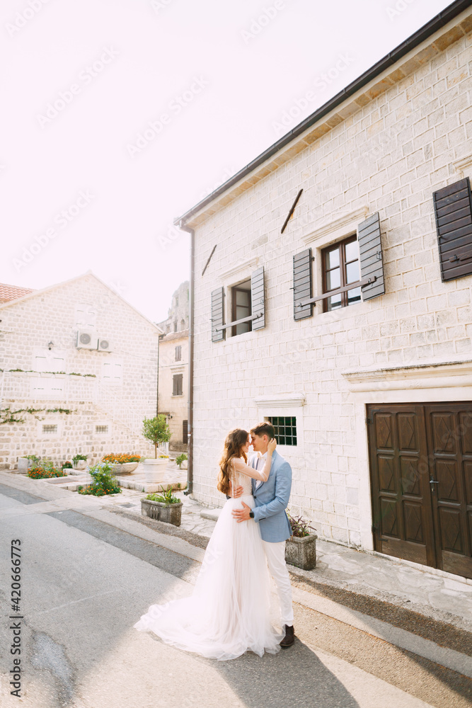 The bride and groom are embracing near the beautiful white house in the old town of Perast 