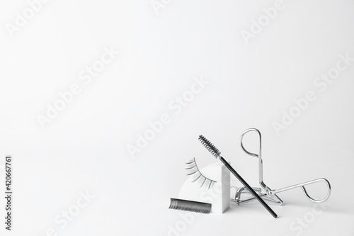 Composition with false eyelashes, curler and brush on light background