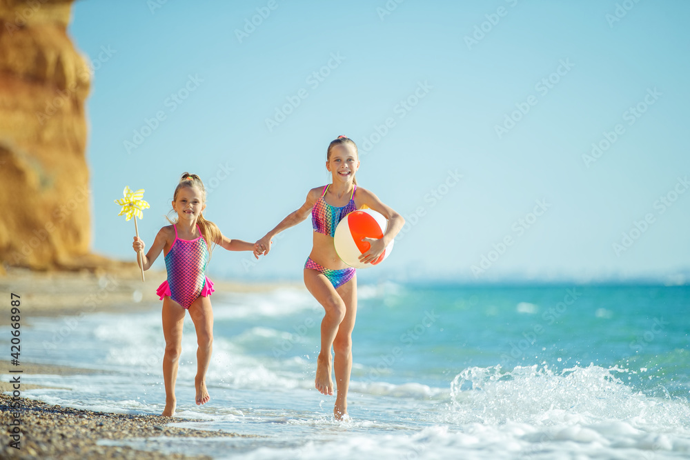 Children at sea play merrily. Two sisters run, jump on the beach in summer. High quality photo.