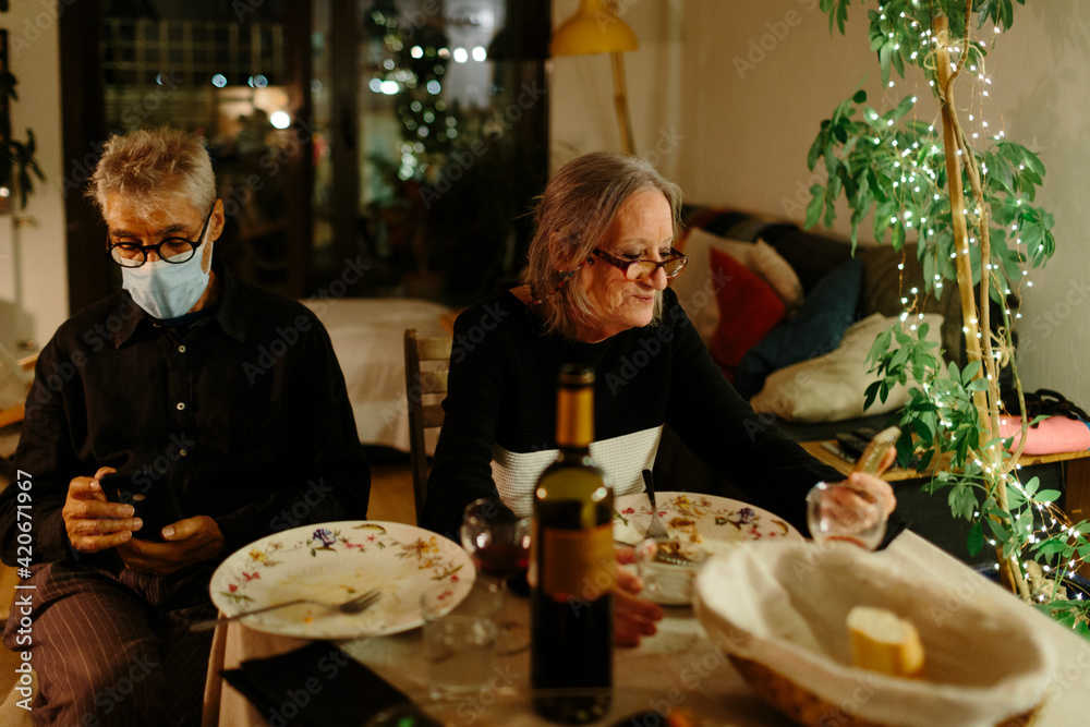 Elderly couple checking their smart phones after dinner at home at night