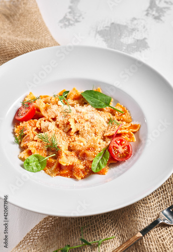 Farfalle pasta food on white table. Pasta restaurant plate with basil leaf and tomato, red tomato sauce. Delicious italian pasta.