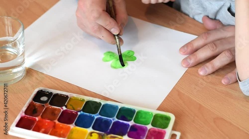 Dad and son drawing a leaf of clover on a white sheet of paper with paintbrush and watercolors.Hands close up.Concept of St.Patrick's Day.Joint family leisure.