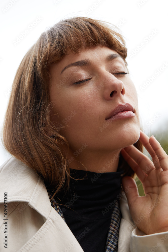 Woman standing outside touching her cheek Woman standing outside touching her cheek