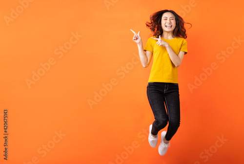Young asian girl jumping up on orange background