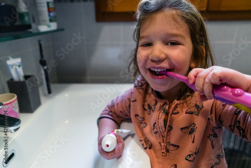 Happy little girl brushing teeth in bathroom photo