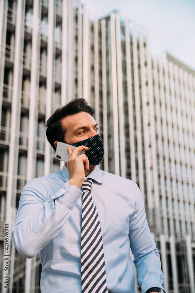Businessman in protective mask talking on phone in city Businessman in protective mask talking on phone in city