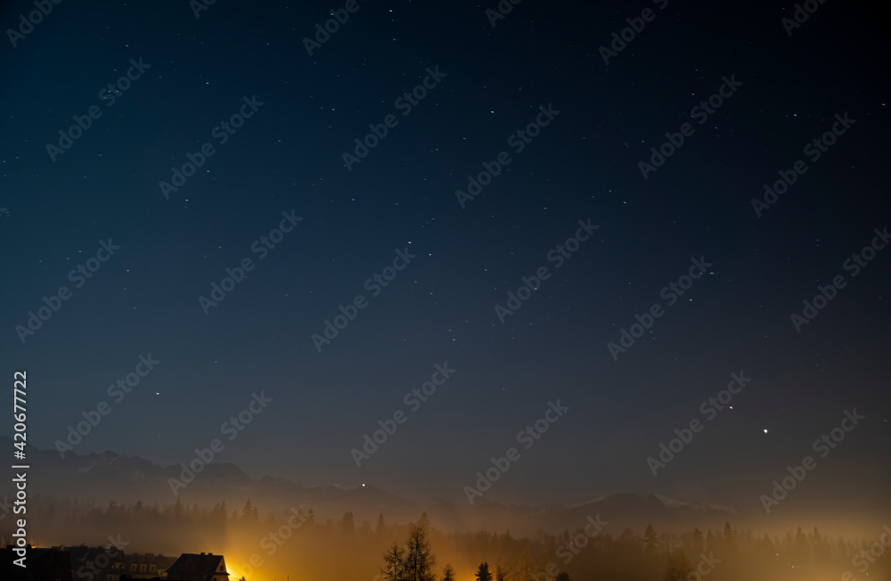 Starry night sky in Poronin, Poland. Tatra Mountain silhouette can be seen in the distance. Selective focus on the ridge, blurred background.