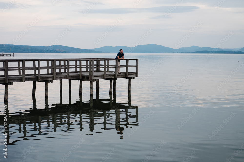 Man relaxing on a pier looking out at a calm lake. Man relaxing on a pier looking out at a calm lake.