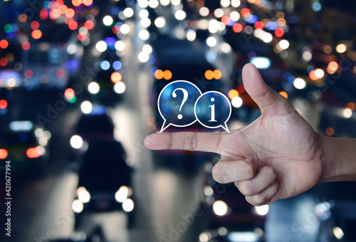 Question mark and information chat icon on finger over blur colorful night light traffic jam road with cars in city, Business customer service and support online concept