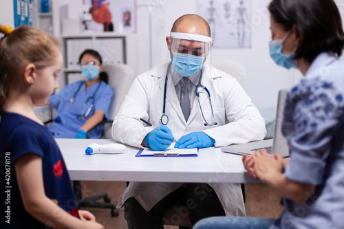 Specialist doctor wearing protective mask and gloves against covid19 writing medical expertise. Healthcare practitioner in medicine providing professional radiographic treatment in hospital clinic