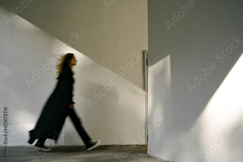 Woman in black coat walking fast near wall photo