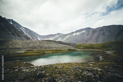 Scenic alpine landscape with turquoise glacial lake among mountains under cloudy sky. Atmospheric scenery with transparent mountain lake in rainy weather. Beautiful clear mountain lake among rocks.