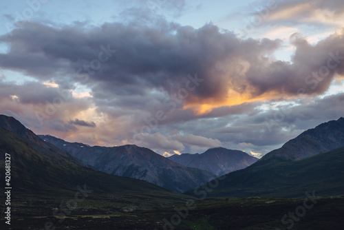 Beautiful mountain scenery with golden dawn light in cloudy sky. Scenic mountain landscape with illuminating color in sunset sky. Silhouettes of mountains on sunrise. Gold illuminating sunlight in sky © Daniil