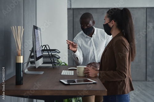 Smart diverse businesspeople in masks using desktop computer