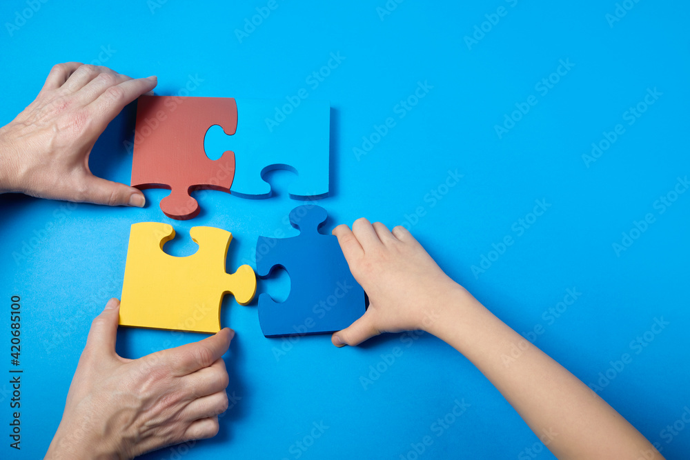 Top view hands of a autistic child and father arranging color puzzle symbol of awareness for autism spectrum disorder. Autism Awareness Day or month. Top view hands of a autistic child and father arranging color puzzle symbol of awareness for autism spectrum disorder. Autism Awareness Day or month.