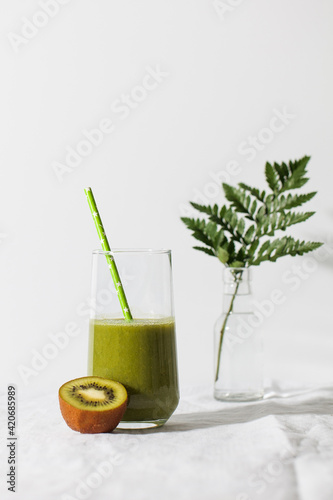 Green smoothie in a glass with a straw and kiwi on a light background. The concept of healthy eating. Copy space.
